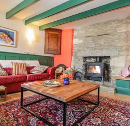 A living room with a red sofa colorful cushions a wooden coffee table a rug and a stone fireplace at Trewenna Roseland Tregony