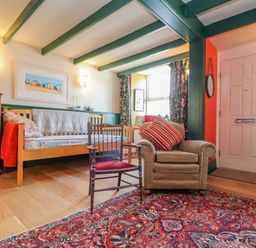 A living room with an armchair and wooden chair on a patterned rug and a sofa with books on shelves at Trewenna Roseland Tregony