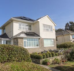 A two-story house with solar panels on the roof and a garden with trimmed bushes and outdoor furniture at Awelfryn in Criccieth