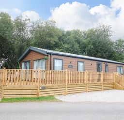 A wooden cabin with a raised deck and railing surrounded by trees at Barneys Retreat in Carnforth