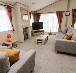 A living room with two grey sofas orange and blue cushions a coffee table tv on a stand and windows with orange curtains at Barneys Retreat in Carnforth