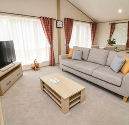 A living room with a gray sofa and cushions next to a wooden coffee table and a television on a wooden stand at Barney's Retreat in Carnforth
