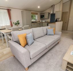 A living room with a gray sofa and cushions next to a wooden coffee table and dining table at Barney's Retreat in Carnforth