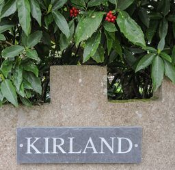 A stone wall with a slate plaque reading Kirland green leaves and red berries behind the wall