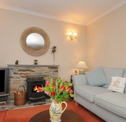 A living room with a stone fireplace a round mirror a television a vase with flowers and a sofa with cushions at Kirland in St Kew Highway