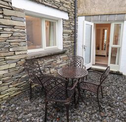 A stone patio with metal table and four chairs outside a house with open glass door at Jennys in Hawkshead