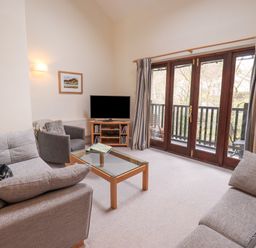 A living room with sofas a glass coffee table a TV and glass doors leading to a balcony at Beechside in Ambleside