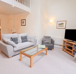 A living room with a sofa and armchair a glass coffee table and a TV on a wooden stand at Beechside Ambleside