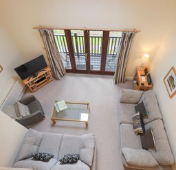 A living room with two sofas an armchair a glass coffee table a television and doors leading to a balcony at Beechside in Ambleside