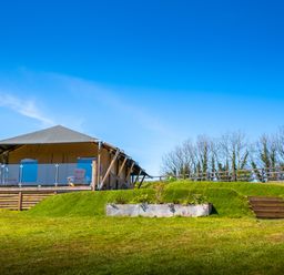 An outdoor tent structure with a deck and chairs on a grassy hill with stairs and a planter box at Semira Tent Lodge in Blackawton