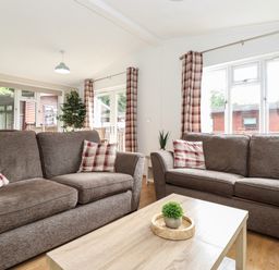 A living room with two brown sofas with plaid cushions and a wooden coffee table at Honeysuckle Lodge in Thirlmere 14 White Cross Bay near Windermere