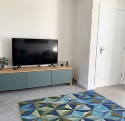 A living room with a television on a cabinet and a geometric patterned rug on the floor at 2 Boathouse Terrace in Mawgan Porth