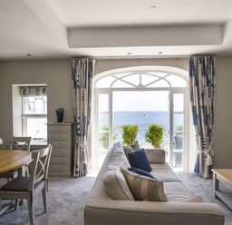 A living room with a beige sofa blue pillows wooden dining table chairs and a view of the sea through large windows at 1 Argyle House Lyme Regis