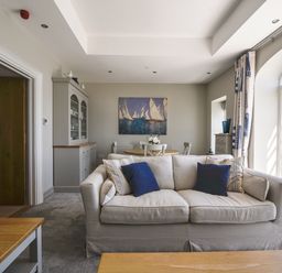 A living room with a sofa and blue pillows a dining table with chairs and a painting of sailboats on the wall at 1 Argyle House in Lyme Regis