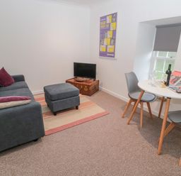 A living room with a sofa ottoman television on a vintage trunk dining table with chairs at Cherry Studio in Crookham near Cornhill-On-Tweed