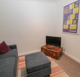 A small living room with a gray sofa and ottoman on a striped rug a TV on a wooden trunk and a framed poster on the wall at Cherry Studio in Crookham near Cornhill-On-Tweed