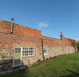 A brick and stone house with windows and a door on a grassy lawn at Cherry Studio in Crookham near Cornhill-On-Tweed