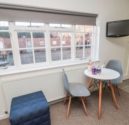 A small dining area with a round white table two gray chairs a blue stool a bottle of wine and two wine glasses by a window at Silverbirch in Crookham near Cornhill-On-Tweed