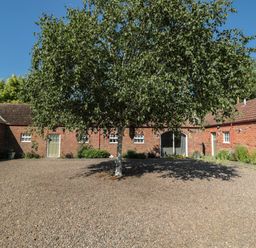 A courtyard area with a tree in the center surrounded by brick buildings at Silverbirch in Crookham near Cornhill-On-Tweed