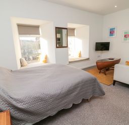 A bedroom with a bed covered with a gray quilt near two window seats and a small sitting area with a sofa and a wooden coffee table at Cheviot View in Crookham near Cornhill-On-Tweed