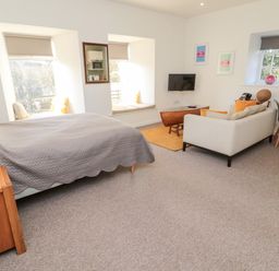 A bedroom with a bed a sofa a wall-mounted TV and two windows with seats at Cheviot View in Crookham near Cornhill-On-Tweed