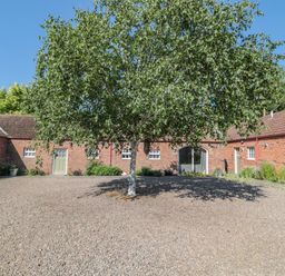 A gravel courtyard with a tree in the center surrounded by single-story brick buildings at Flodden in Crookham near Cornhill-On-Tweed