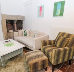 A seating area with a cream sofa and striped armchair next to a stone fireplace at Bakers Cottage in Crookham near Cornhill-On-Tweed