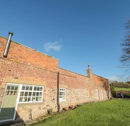 A brick and stone cottage with windows and a green door on a grassy lawn with cars and trees at Bakers Cottage Crookham near Cornhill-On-Tweed