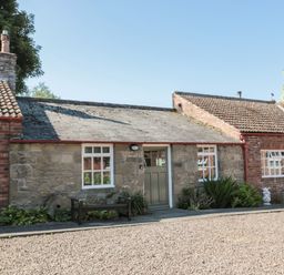 A stone and brick cottage with green doors and windows a bench and plants outside at Bakers Cottage in Crookham near Cornhill-On-Tweed