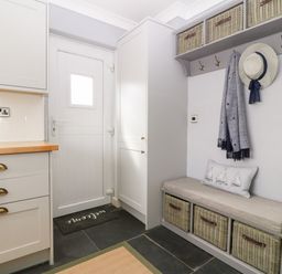 A small entryway with a white door a bench with baskets hooks with a hat and scarf and kitchen cabinets at Valley Pines in Valley