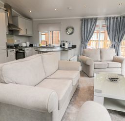 A living room with two sofas a coffee table and a kitchen in the background at Woodpecker Lodge in Highampton near Sheepwash