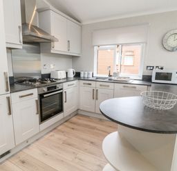 A kitchen with white cabinets a gas stove an oven a microwave and a window with a roller blind at Woodpecker Lodge in Highampton near Sheepwash