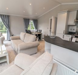 An open living room and kitchen with beige sofas dining table and kitchen appliances at Woodpecker Lodge in Highampton near Sheepwash