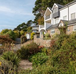 A residential building with white walls and stone accents surrounded by bushes and trees at 14 St Elmo Court in Salcombe