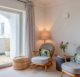A sitting area with two chairs with cushions a lamp a side table with flowers and a woven ottoman near sliding glass doors at 14 St Elmo Court in Salcombe