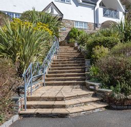 Stone steps with metal railings surrounded by green plants leading up to a white building at 14 St Elmo Court in Salcombe