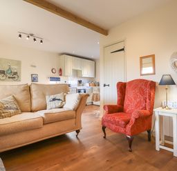 A living room with a beige sofa and red armchair next to a white side table and lamp at The Old Dairy in Colyton