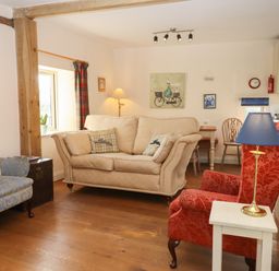 A living room with three armchairs one beige one red and one blue wooden floor and a small table with a lamp at The Old Dairy in Colyton