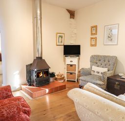 A living room with a wood burning stove armchairs a small television and framed pictures on the walls at The Old Dairy in Colyton