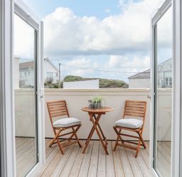 A balcony with two wooden chairs and a round wooden table with plants at 9 Lon Y Dryw in Trearddur Bay