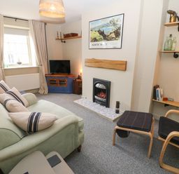 A sitting room with a green sofa and armchair around a fireplace and a corner TV unit at Llety Bach in Caernarfon