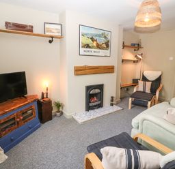 A living room with a TV on a wooden cabinet a fireplace and seating at Llety Bach in Caernarfon