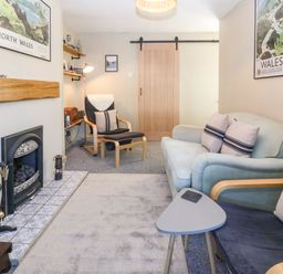 A sitting room with armchairs a sofa a fireplace and a wooden sliding door at Llety Bach in Caernarfon