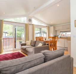 An open living and dining area with gray sofas a red rug a wooden dining table and a kitchen with white cabinets at Garuda Calgarth 19 White Cross Bay near Windermere