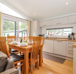 A dining area with a wooden table and chairs next to a kitchen with white cabinets and a window at Garuda Calgarth 19 White Cross Bay near Windermere