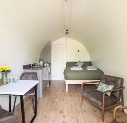 A small curved room with a bed at the end a kitchenette on the left and a table with chairs and armchairs at Tyddyn Parthle Pod 1 in Bontnewydd Gwynedd