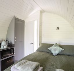 A small room with a bed covered with green bedding next to a kitchenette with a microwave and a fridge at Tyddyn Parthle Pod 1 in Bontnewydd Gwynedd