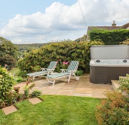 An outdoor patio with two striped lounge chairs a hot tub and surrounding greenery at The Gables in Sheepscombe