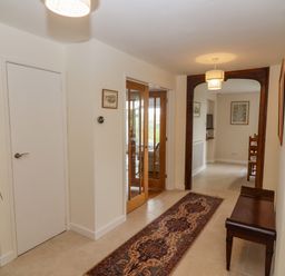 A hallway with a patterned runner rug a wooden bench wooden framed glass doors and framed pictures on cream walls at The Gables in Sheepscombe