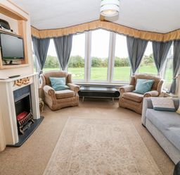 A living room with two armchairs and a sofa around a fireplace with a TV mounted above at Plas Tirion Caravan Llanfairynghornwy near Cemaes Bay